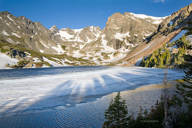 Sunrise casts shadows over thawing ice on Lake Isabelle, Indian Peaks Wilderness, Colorado.